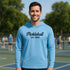 Man wearing a blue hoodie with 'Pickleball Est. 1965' text on a pickleball court.